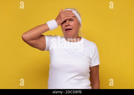 Ältere kaukasische Frau müde Reiben Kopf nach dem Training erschöpft. Stress und Frustration Konzept. Stockfoto