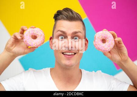 Schöner blonder Mann auf buntem Hintergrund hält zwei rosa Donuts Stockfoto