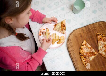 Junges Mädchen saß am Küchentisch essen Huhn Nuggets und Pizza Stockfoto