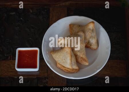 Samosas auf einem weißen Teller mit dippender würziger roter Sauce Stockfoto