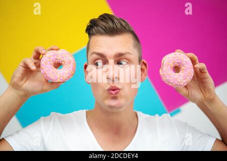 Schöner blonder Mann auf buntem Hintergrund hält zwei rosa Donuts Stockfoto