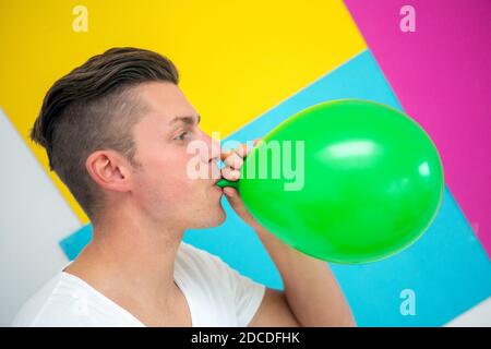 Schöner blonder Mann hält einen grünen Ballon auf buntem Hintergrund Stockfoto