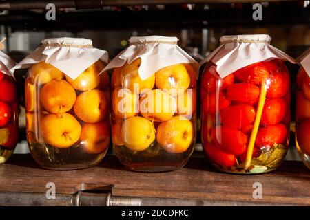 Große Gläser mit eingelegten Äpfeln und Tomaten auf einem Vintage-Regal. Hausgemachter Saft aus der Dose Stockfoto