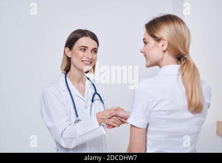 Professionelle Ärztin Frau schüttelt die Hand einer Patientin an Ein heller Hintergrund Stockfoto