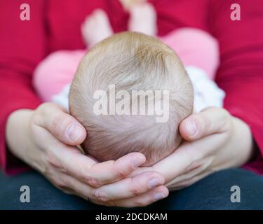 Mutter liebevoll hält neugeborenes Mädchen auf ihrem Schoß mit Ihr Kopf in den Händen und winzige Füße berühren sie Bauch Stockfoto