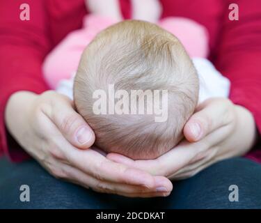 Mutter liebevoll hält neugeborenes Mädchen auf ihrem Schoß mit Ihr Kopf in den Händen und winzige Füße berühren sie Bauch Stockfoto