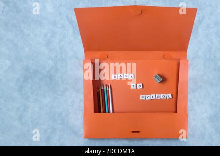 Eine Frontansicht von oben auf eine offene orangefarbene Mappe mit Buntstiften, einem Bleistiftspitzer, einem Mosaikbuchstabe mit dem Satz "zurück zur Schule". Stockfoto