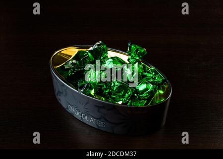 Schachtel mit Süßigkeiten in grünen Folienverpackungen auf schwarzem Hintergrund. Stockfoto