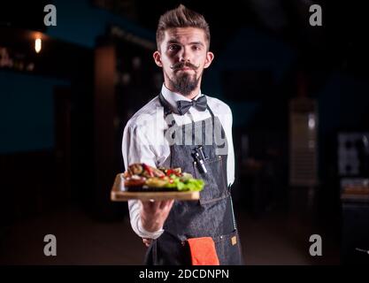 Im Restaurant serviert ein junger Kellner sehr hilfsbereit Gerichte. Stockfoto