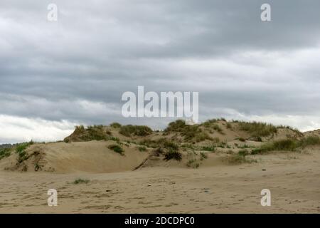 Ein leerer Strand mit hohen Sanddünen unter einem bedeckten Himmel Stockfoto