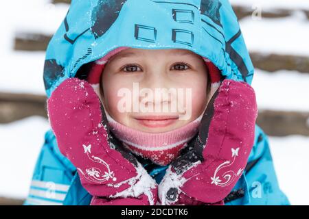 Nahaufnahme Porträt von niedlichen kaukasischen Baby in Winterkleidung. Ein 6-7-jähriges Mädchen mit ruddigen Wangen aus Frost, im Winter Overalls und Fäustlinge Stockfoto