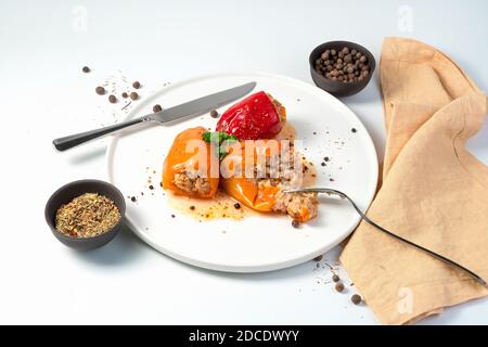 Gericht mit Paprika mit Fleisch und Reis auf einem weißen Teller mit Gewürzen, Besteck und Serviette auf hellem Hintergrund. Stockfoto