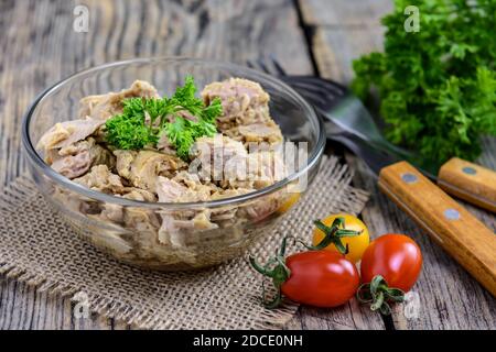 Portion Thunfischsalat mit frischer Petersilie, Kirschtomate und zwei Gabeln auf rustikalem Holztisch. Selektiver Fokus. Stockfoto