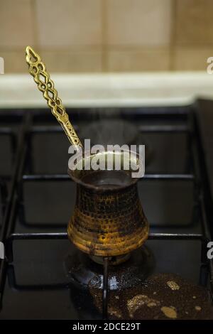 Zubereitung von Kaffee in einem türke auf einem Gasherd. Traditionelle kupferfarbene türkische Kaffeekanne, Cezve, Ibrik. Gasherd mit verschüttetem Kaffee. Stockfoto