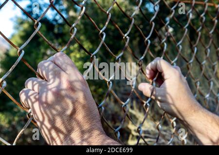 Die Hände von Mans halten sich am Kettengliederzaun fest Stockfoto