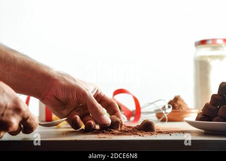 Hände setzen Kakao in hausgemachte Trüffel für eine Veranstaltung isoliert Hintergrund. Vorderansicht. Horizontale Zusammensetzung. Stockfoto