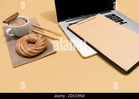 Laptop, Kuchen, Tasse Tee und Lebenslauf Blatt auf dem pastellorange Tisch, Draufsicht. Stockfoto