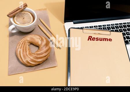 Laptop, Kuchen, Tasse Tee und Lebenslauf Blatt auf dem pastellorange Tisch, Draufsicht. Stockfoto