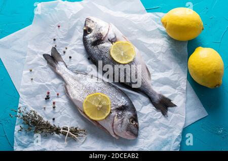 Frischer, roher Fisch mit Zitronenscheiben, Kräutern und Pfeffer auf blauem Hintergrund. Gesundes Lebensmittelkonzept, Draufsicht. Stockfoto