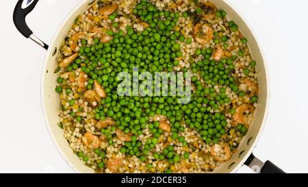 Garnelen, Orzo, Couscous und grüne Erbsen schließen auf Bratpfanne auf weißem Hintergrund direkt von oben Stockfoto