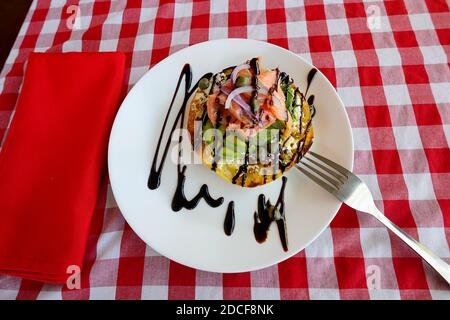 Geräucherter Gourmet-Lachs, Avocado, Kapern, rote Zwiebeln und Toast auf einem weißen Teller serviert, garniert mit Balsamico-Dressing Stockfoto