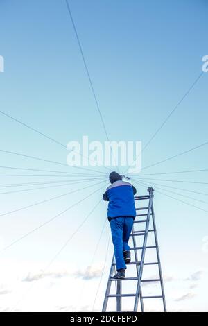 Elektriker repariert elektrische Verkabelung auf dem Dach eines Hochhauses, das auf der Treppe gegen den blauen Himmel steht. Speicherplatz kopieren Stockfoto