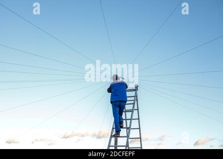 Elektriker repariert elektrische Verkabelung auf dem Dach eines Hochhauses, das auf der Treppe gegen den blauen Himmel steht. Speicherplatz kopieren Stockfoto