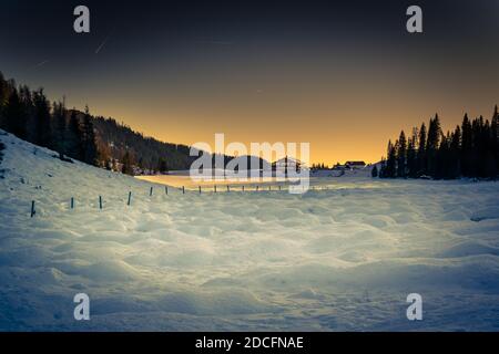 Winterpanorama des Calaita Sees bei Dämmerung. Gefrorener See, Tannenwälder und verschneite Wiesen. Lozental, Trentino-Südtirol Stockfoto