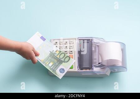 Online-Shopping-Konzept. Nahaufnahme eines Kinderhands mit einer 100-Euro-Banknote über der Kasse auf blauem Hintergrund, Draufsicht, Kopierraum. Stockfoto