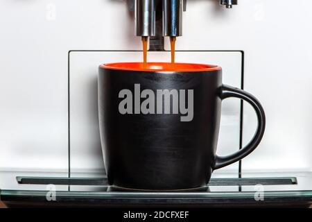 Kaffee geht aus einer Kaffeemaschine in schwarzem Becher. Vorderansicht, Nahaufnahme. Stockfoto