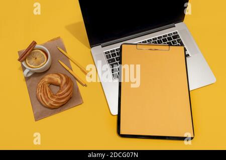 Laptop, Kuchen, Tasse Tee und Lebenslauf Blatt auf der Fortuna Gold Gelb Farbe Hintergrund, Draufsicht. Stockfoto