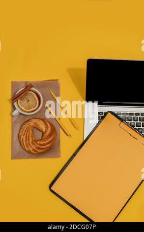 Laptop, Kuchen, Tasse Tee und Lebenslauf Blatt auf der Fortuna Gold Gelb Farbe Hintergrund, Draufsicht. Stockfoto