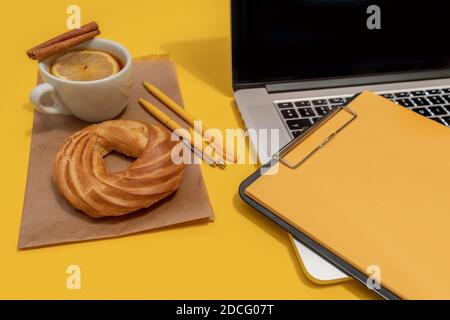 Laptop, Kuchen, Tasse Tee und Lebenslauf Blatt auf der Fortuna Gold Gelb Farbe Hintergrund, Draufsicht. Stockfoto