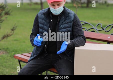 Lieferservice Kurier während der Coronavirus, COVID-19, Pandemie, Lieferung Mann in medizinische Schutzmaske, Handschuhe Sprühen Alkohol Desinfektionsmittel spr Stockfoto