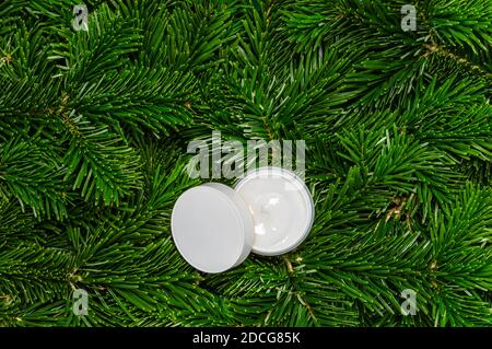 Weiße offene Creme Glas oder Körperlotion auf Tannenbaum Zweige Hintergrund. Natürliches organisches kosmetisches Produkt. Winterpflege und Spa-Behandlung Stockfoto