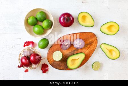 Avocado Hälften, Limetten und Zwiebeln - Grundzutaten Guacamole auf weißem Arbeitsbrett, flach Lay Foto Stockfoto