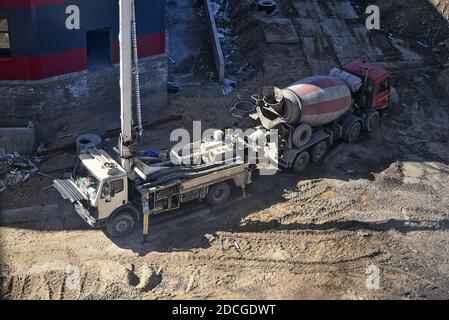 Schwere Betonmischer und Betonpumpe warten auf ihre Arbeit auf der Baustelle. Lieferung von Beton und Gießen von Beton Stockfoto