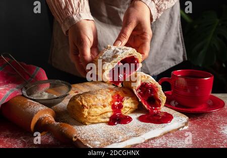 Weibliche Hände backt einen Puff mit Pflaume oder rote Johannisbeermarmelade auf dem Tisch. Stockfoto