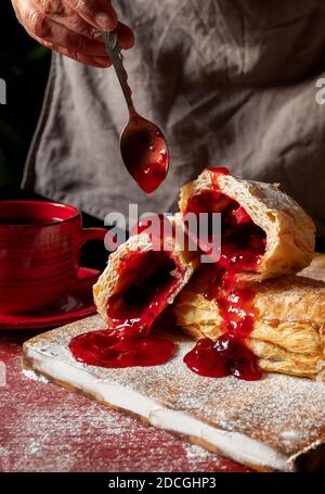 Weibliche Hände backt einen Puff mit Pflaume oder rote Johannisbeermarmelade auf dem Tisch. Stockfoto