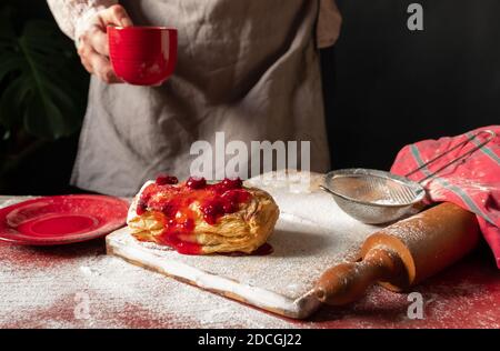 Weibliche Hände halten rote Tasse Kaffee in der Nähe von Puff mit Pflaume oder rote Johannisbeermarmelade auf dem Tisch besetzt. Stockfoto