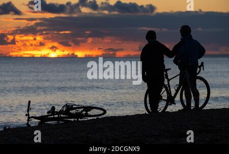 Silhouetten eines (männlichen) Personenpaares, das das Familienkonzept von Vater und Sohn illustriert, am Strand, wo man einen Sonnenuntergang beobachtet, während die Sonne über dem Meer untergeht. Stockfoto
