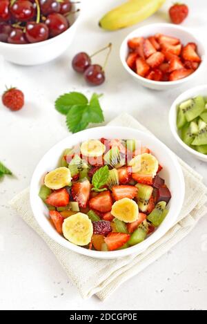 Gesundes Frühstück mit Obstsalat aus Erdbeere, Kiwi und Banane auf hellem Steingrund Stockfoto