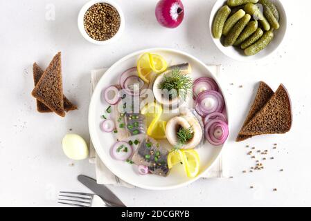 Gesalzener Hering mit Zwiebeln und Zitrone auf Teller auf weißem Steingrund. Russische Küche. Draufsicht, flaches Lay Stockfoto