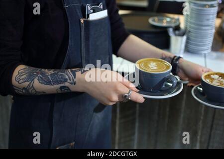 Großbritannien / England / London / Bariasta mit Tattoo serviert flachen weißen Kaffee in einem trendigen Café . Stockfoto