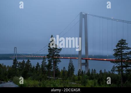 Bild der beleuchteten Höga Kustenbron, einer Hängebrücke über den Fluss Ångermanälven bei Veda, Schweden, an einem späten Abend in tiefen Wolken. Stockfoto