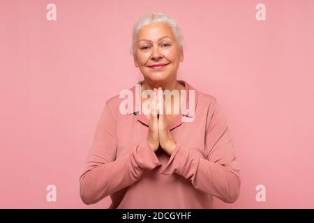 Ältere kaukasische Frau, die die Handflächen vor sich zusammengedrückt hält, um Vergebung bittet und sich traurig fühlt. Studio auf rosa Wand aufgenommen. Stockfoto