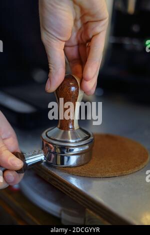 Nahaufnahme der Hände, Barista drück gemahlenen Kaffee mithilfe eines Sabotagegriffs in den Portafilter, um einen Espresso zu einem heißen Getränk zu machen Stockfoto