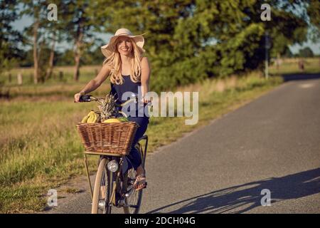 Porträt einer schönen Frau lächelnd glücklich, während sie ein gestreiftes Hemd trägt und ein Fahrrad in der Landschaft an einem sonnigen Tag fährt Stockfoto