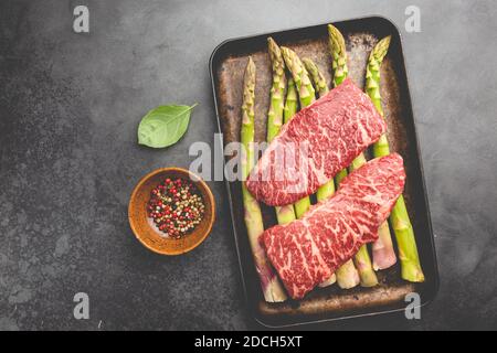 Rohes Steak mit grünem Spargel auf Tablett auf schwarzem Hintergrund, Draufsicht Stockfoto