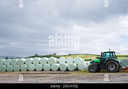 Heuballen, die von Landwirt und Traktor auf dem Feld gerollt werden Für die Ernte Stockfoto